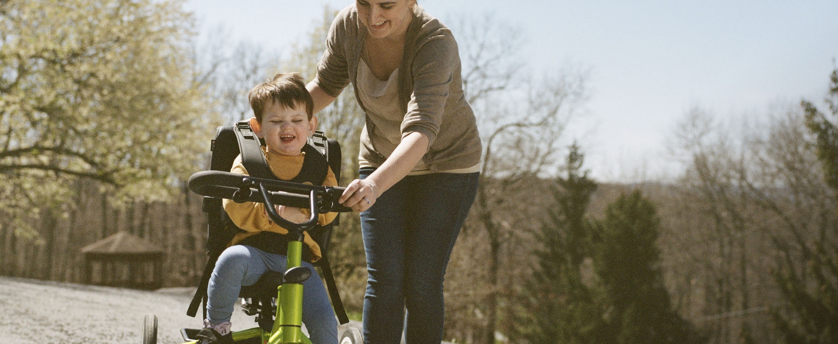 Diana pushing Lina on a tricycle outdoors